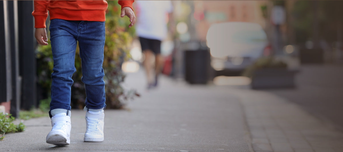 Child walking down a sidewalk in GILi Guise denim jeans and white sneakers
